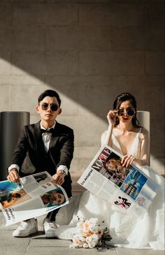 a man and woman sitting on the ground with newspapers in front of them, both holding photos