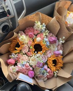 a bouquet of sunflowers and other flowers in a brown paper bag on the dashboard of a car