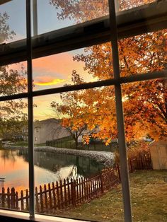 the view from an open window looking out onto a lake and trees with orange leaves