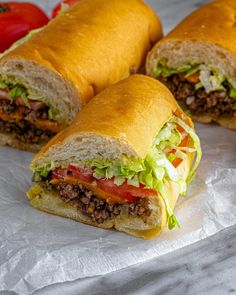 two sandwiches cut in half sitting on top of white paper next to tomatoes and lettuce