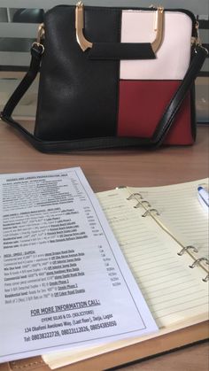 a black, white and red purse sitting on top of a table next to an open book