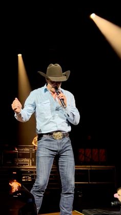 a man standing on top of a stage wearing a cowboy hat and holding a microphone