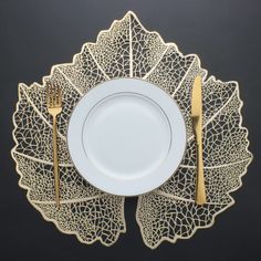 a white plate with gold cutlery on it next to a leaf shaped placemat