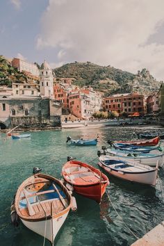 several small boats are docked in the water near some houses and buildings on the shore