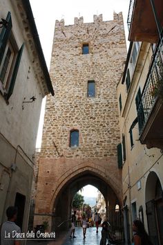 people are walking down an alley way between two buildings with stone walls and arched doorways