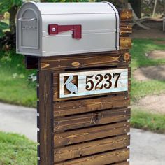 a wooden mailbox sitting on the side of a road next to some grass and trees