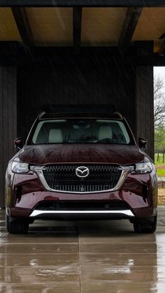 the front end of a maroon car parked in a garage with rain falling on it