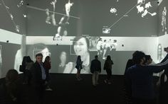 people are standing in an art gallery looking at images projected on the walls and ceiling