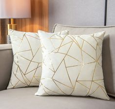 two white pillows sitting on top of a gray couch next to a lampshade