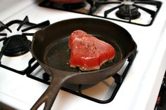 a piece of meat is being cooked in a skillet on the stove with other cooking utensils