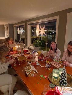 a group of women sitting around a wooden table with christmas presents on it and candles in the middle