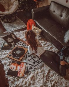 a woman sitting on the floor next to a couch with various records and cds in front of her