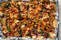 an aluminum pan filled with nachos and vegetables on top of foil covered in seasoning