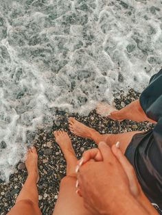 two people are sitting on the beach with their feet in the water and one is holding his hand