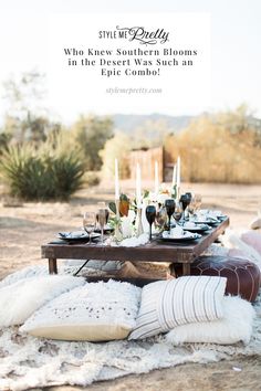 a table set up with candles, plates and wine glasses on a rug in the desert