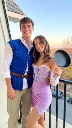 a man standing next to a woman in a purple dress and holding a frying pan