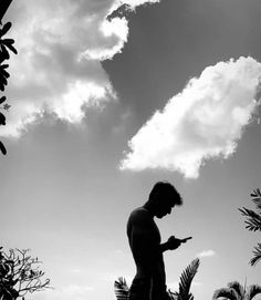 a man standing in front of some trees using his cell phone while looking at the sky