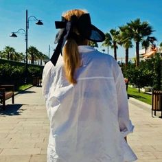 a woman in white shirt and black hat walking down sidewalk with palm trees behind her