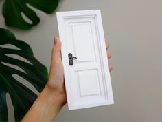 a person holding up a white door with a key in it's middle and palm leaves behind them