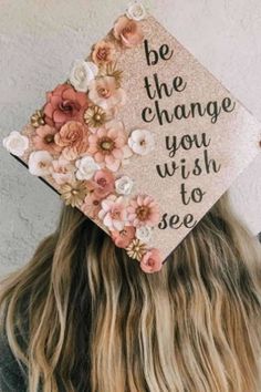 a woman wearing a graduation cap with flowers on it and the words be the change you wish to see