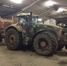 two large tractors are parked in a garage with other vehicles behind them and one is green