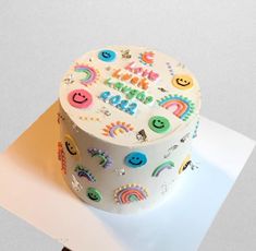 a birthday cake decorated with smiley faces, rainbows and stars on a white surface