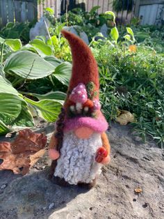 a small gnome figurine sitting on top of a rock in front of some plants