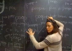 a woman standing in front of a blackboard with writing on it and holding her hair up