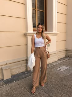 a woman standing in front of a building with her hands on her hips and holding a purse