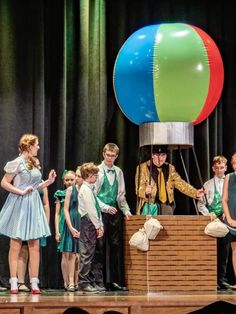 a group of children standing on top of a stage next to an air ballon