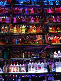 many bottles are lined up on the shelves in a bar with neon lights behind them