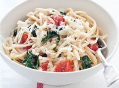 a white bowl filled with pasta and spinach on top of a striped table cloth