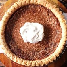 a pie sitting on top of a wooden table next to a white plate with whipped cream