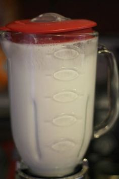 a blender filled with white liquid sitting on top of a kitchen counter next to a red lid