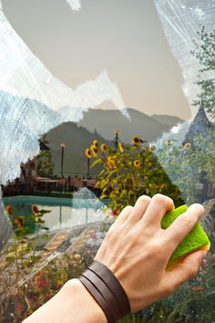 a hand is holding a sponge and cleaning the outside of a window with mountains in the background