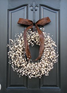 a wreath on the front door with white flowers and brown ribbon hanging from it's side