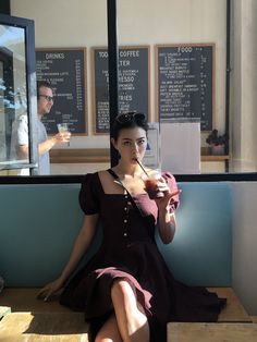 a woman is sitting on a bench with a drink in her hand and drinking from a straw