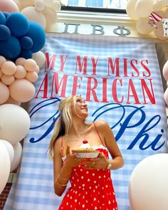 a woman in a red and white dress is holding a piece of cake while standing next to balloons