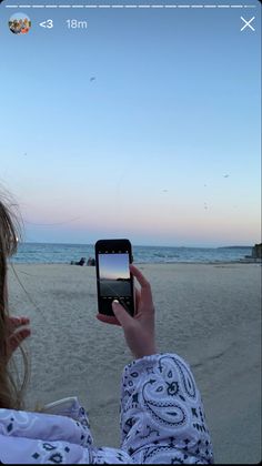 a woman taking a photo with her cell phone on the beach at sunset or dawn