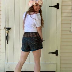 a woman standing in front of a door wearing shorts and a flower crown on her head