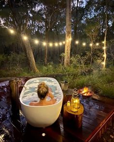 a woman sitting in a large bathtub next to a fire pit with lights strung above it