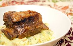 a white bowl filled with meat and mashed potatoes on top of a floral table cloth