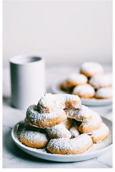 powdered sugar covered donuts on a white plate next to a cup of coffee