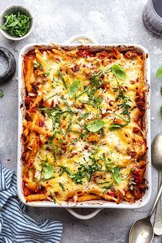 a casserole dish filled with pasta, cheese and spinach sprinkled with herbs