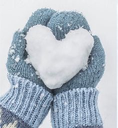 a pair of blue mittens with a white heart in the middle and snow on top