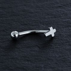 a silver nose ring with a white cross on the end, resting on a black surface