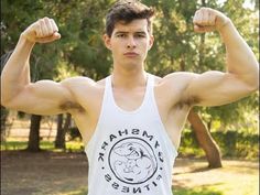 a young man flexing his muscles for the camera with trees in the back ground behind him