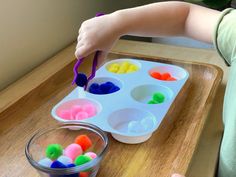 a child is playing with colored pom - poms in a tray on a table