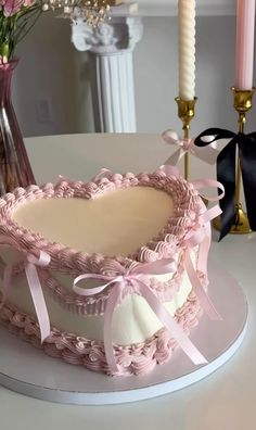 a cake with pink icing and bows on it sitting on a table next to candles