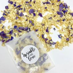 two bags filled with purple and yellow flowers on top of a white tablecloth next to a bag of granola